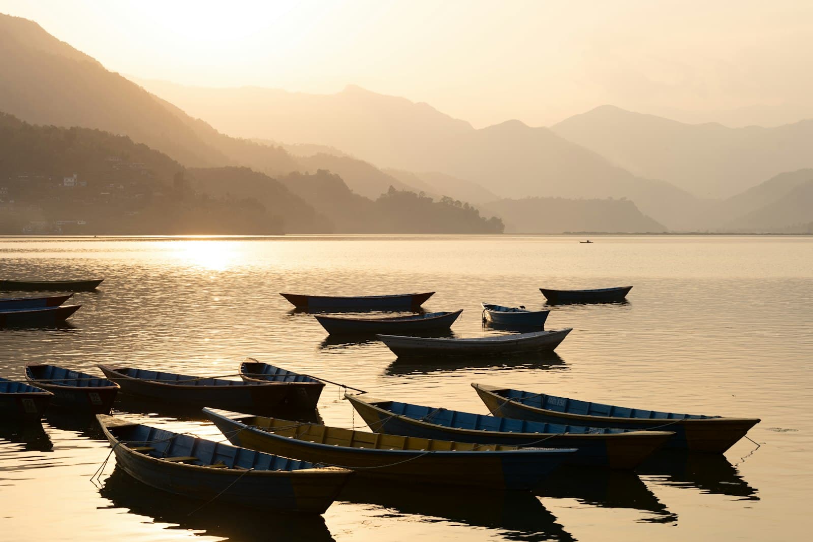 Wooden boats resting on a still, golden, mist-covered lake below silhouetted hills.