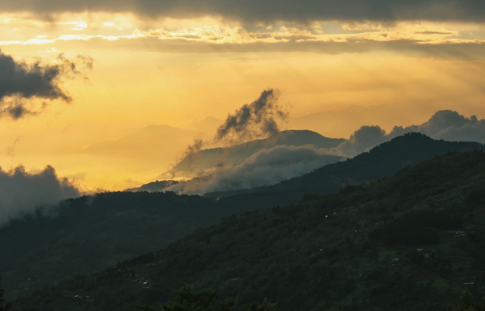 Golden light over layered, mist-wrapped mountain ridges at dusk.
