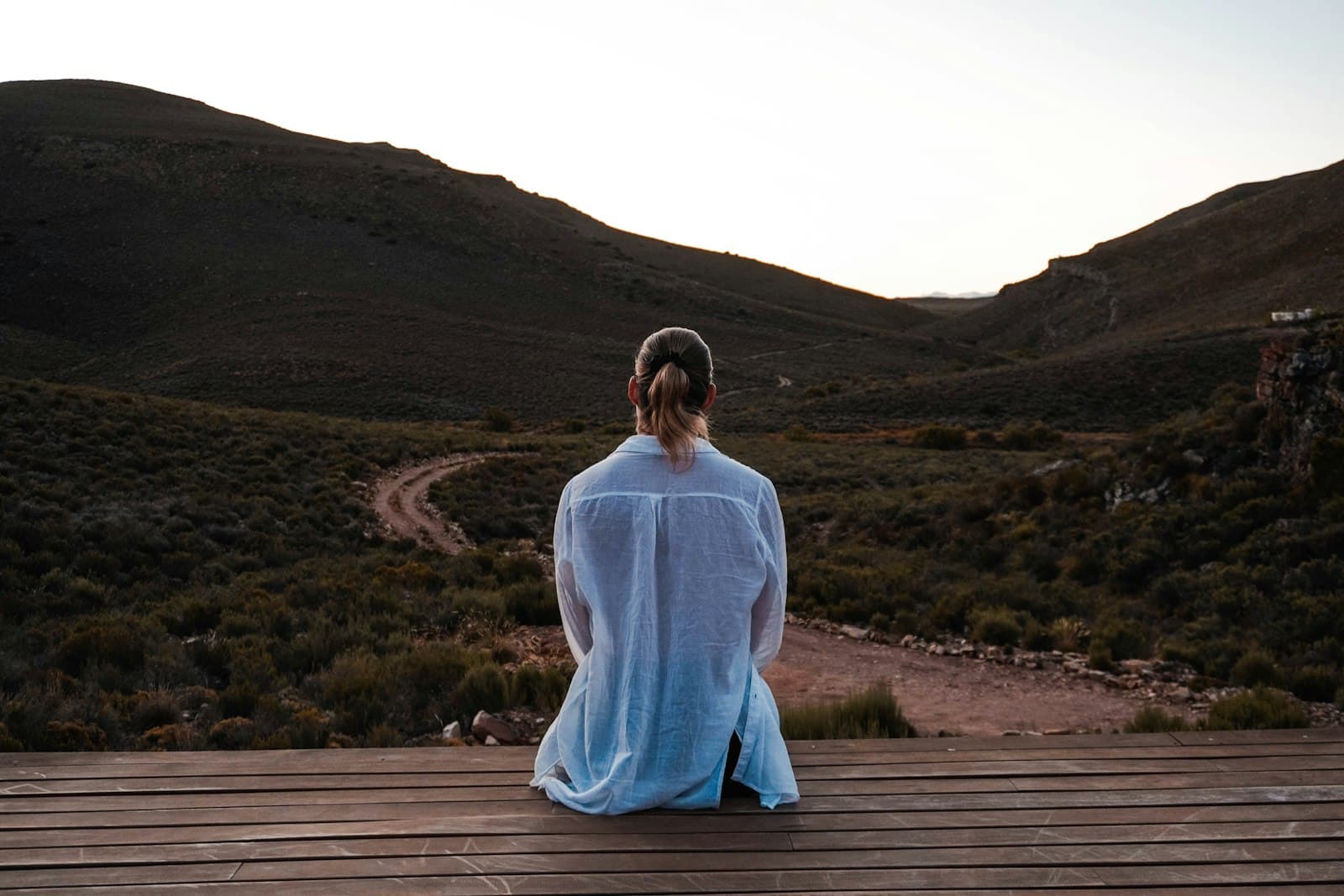 A person seated on a wooden deck, back to camera, looking out over a wide valley.