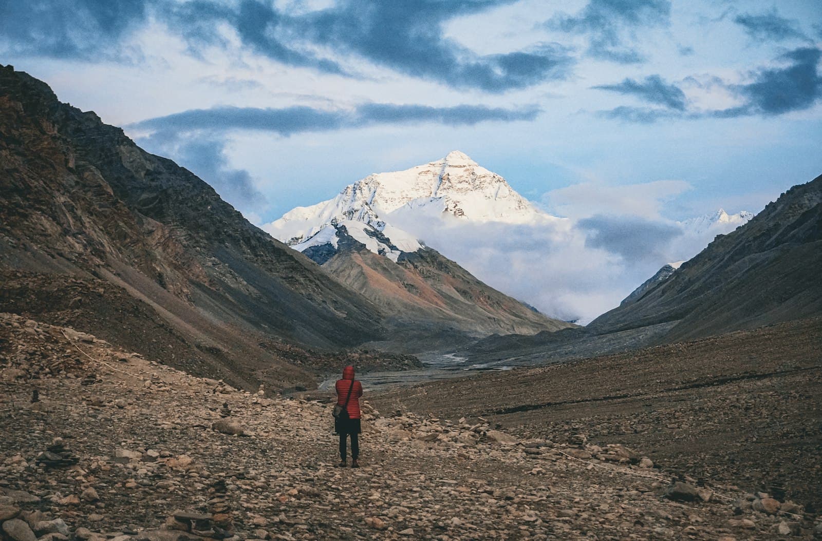 A lone hiker crossing a broad dry valley toward a distant snow-capped peak.